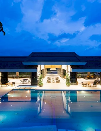A luxurious outdoor pool area at a modern building is lit up in the evening, creating a relaxing ambiance.