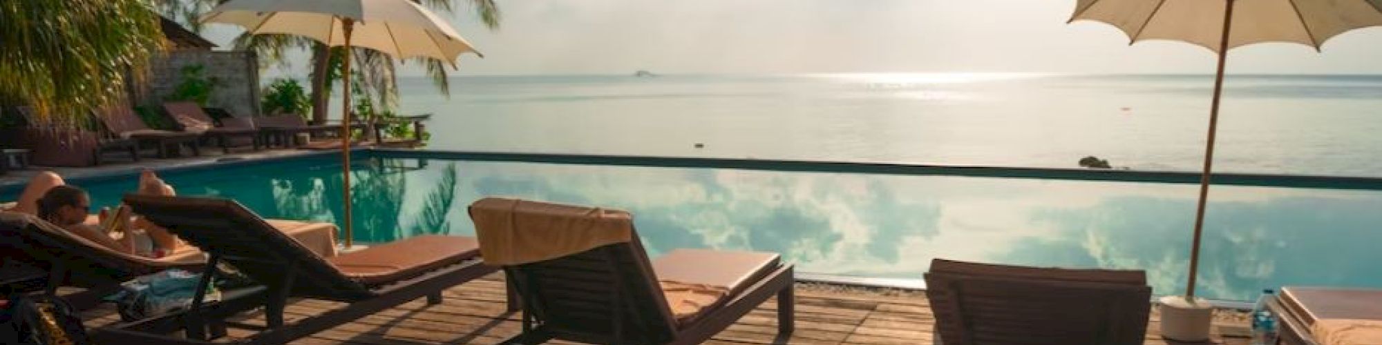A serene poolside scene with lounge chairs, umbrellas, and a stunning view of the ocean under a bright, partly cloudy sky.
