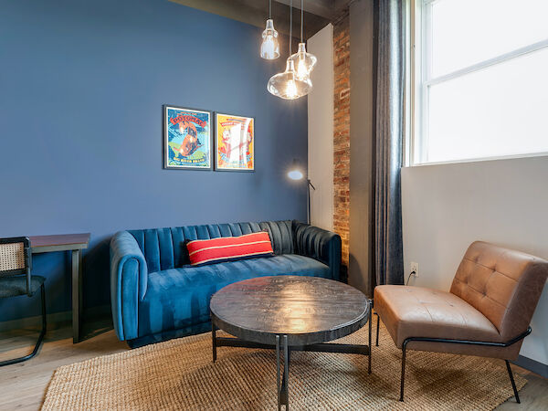 A cozy living room with a blue wall, a blue sofa, a round coffee table, a brown chair, and framed pictures on the wall ends the sentence.