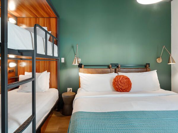 The image shows a well-decorated bedroom with a double bed, a set of bunk beds, green walls, and two wall-mounted bedside lamps.