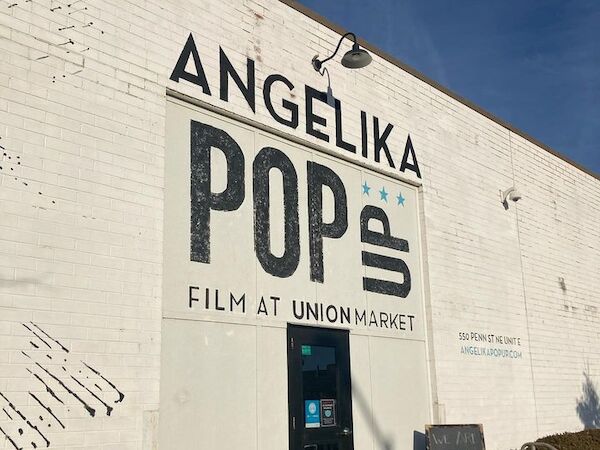 The image shows the exterior of a building with "ANGELIKA POP UP FILM AT UNION MARKET" written on it. There's an entrance door and a sign nearby.