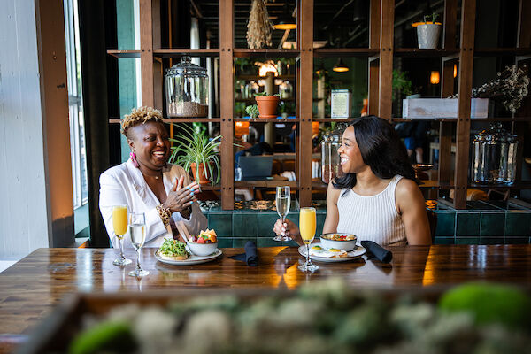 Two people enjoying breakfast in the stylish lobby cafe with plants and shelves in the background.