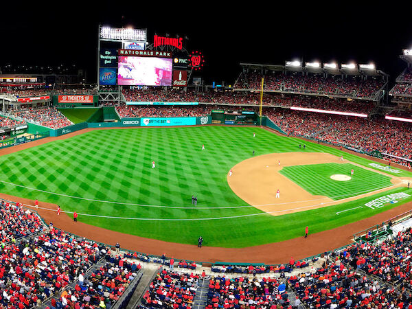 A wide-angle view of a brightly lit baseball stadium at night, filled with a large crowd, showcasing the field and the scoreboard in the background.