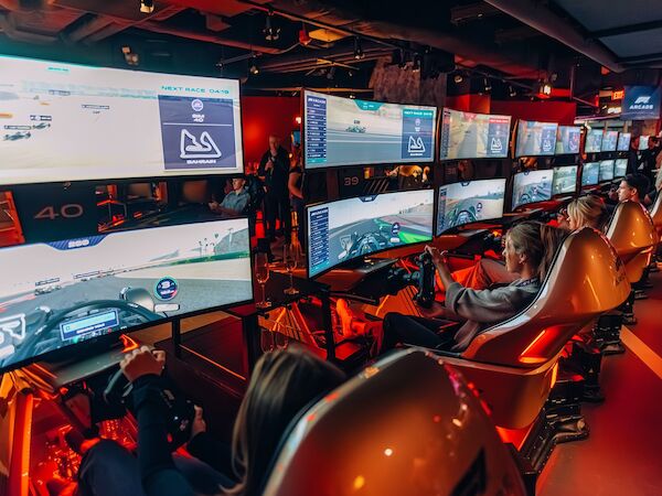 People are engaged in a racing simulation experience with multiple screens and seats resembling a real racing setup.