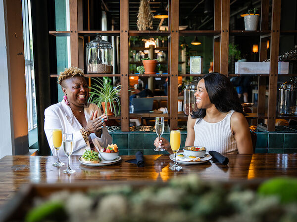 Two people enjoying breakfast in the stylish lobby cafe with plants and shelves in the background.