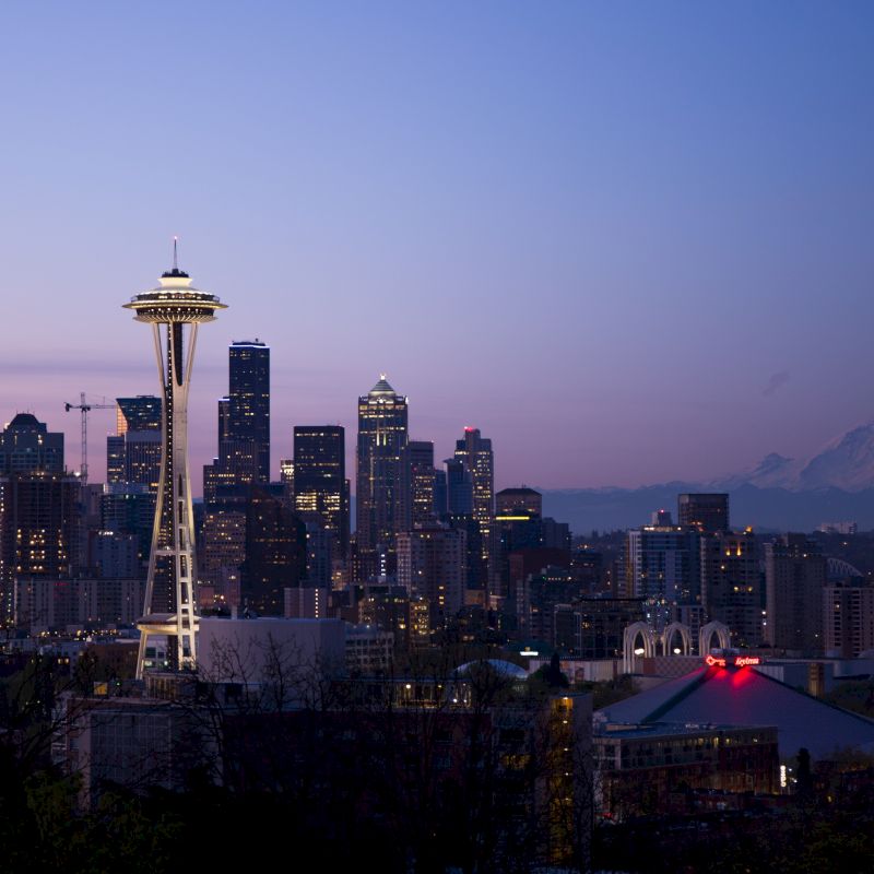 This image shows the skyline of Seattle at dawn or dusk, featuring the Space Needle and Mount Rainier in the background.