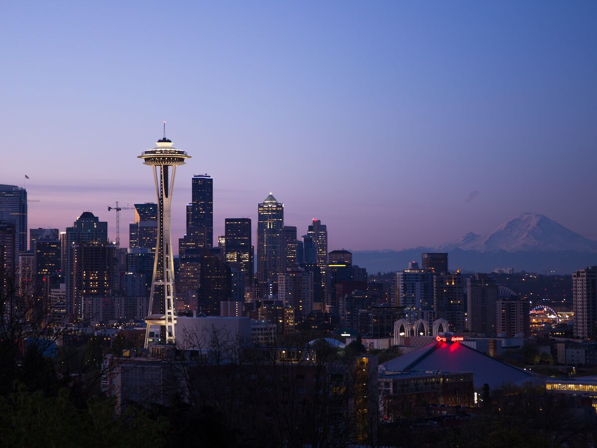 This image shows a city skyline at twilight, featuring the iconic Space Needle in Seattle, with Mount Rainier visible in the background.