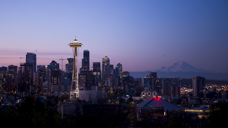 This image shows a city skyline at twilight, featuring the iconic Space Needle in Seattle, with Mount Rainier visible in the background.